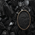 A top-down view of a small round bowl filled with fine black activated charcoal powder, resting on a bed of jagged charcoal chunks with dark, matte textures.